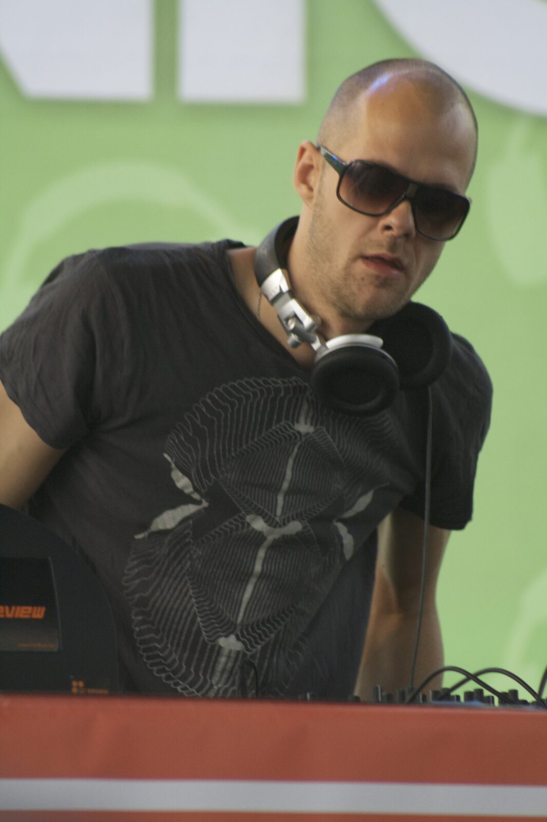 Adam Beyer in dark sunglasses with headphones around his neck, leaning over the DJ booth at the Detroit Electronic Music Festival in 2009