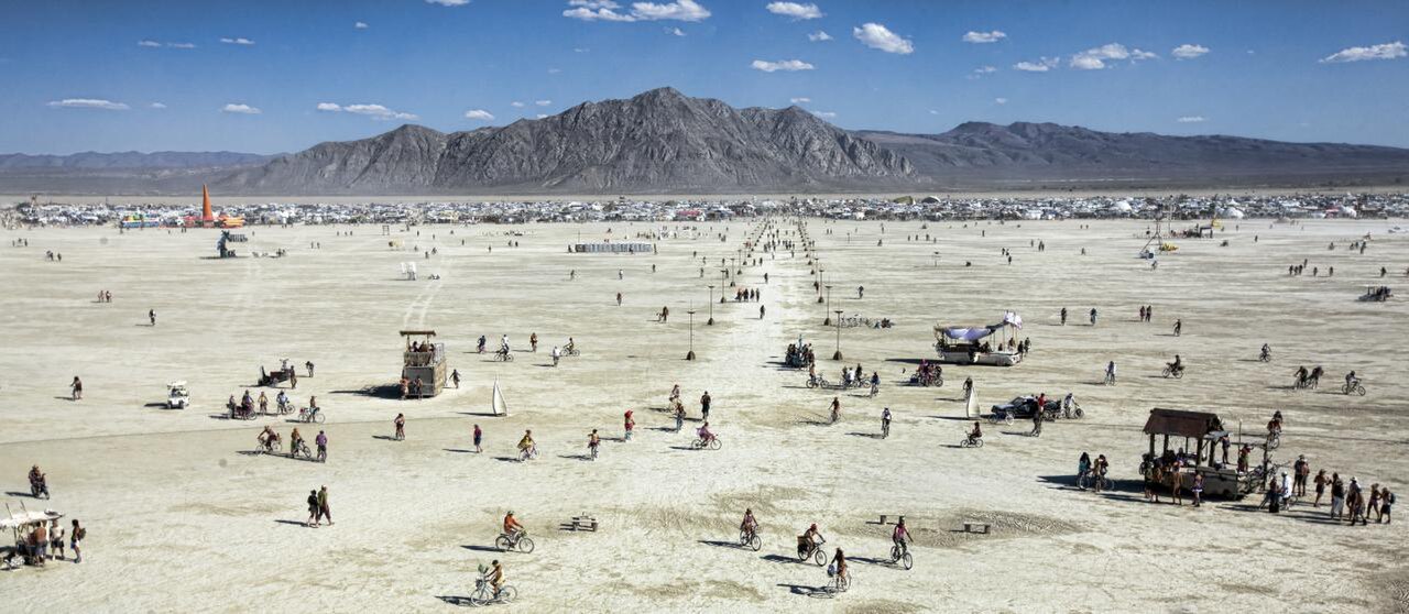 Aerial view of Black Rock City during Burning Man, showing the temporary city's radial street grid on the playa. Photo by Christopher Michel, CC BY 2.0, via Wikimedia Commons.