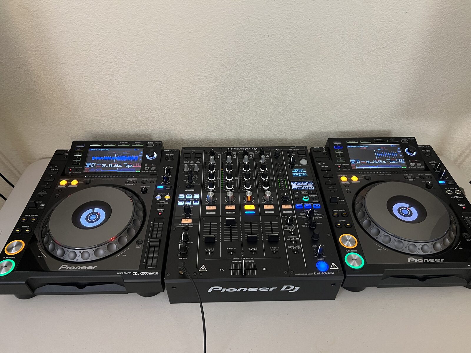 Two Pioneer CDJ-2000 Nexus media players either side of a Pioneer DJ DJM-900 mixer on a table, with the tempo faders at the right edge of each player.