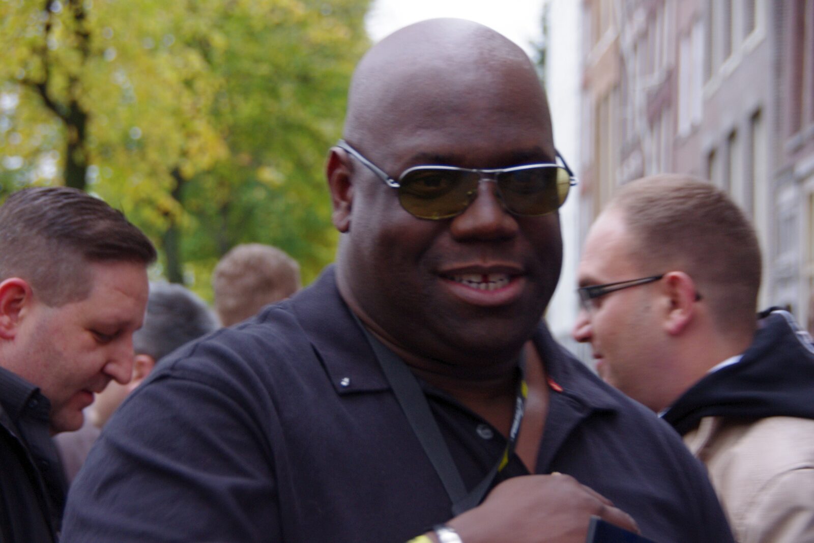 Carl Cox smiling in tinted sunglasses and a dark polo shirt on a street during Amsterdam Dance Event 2012