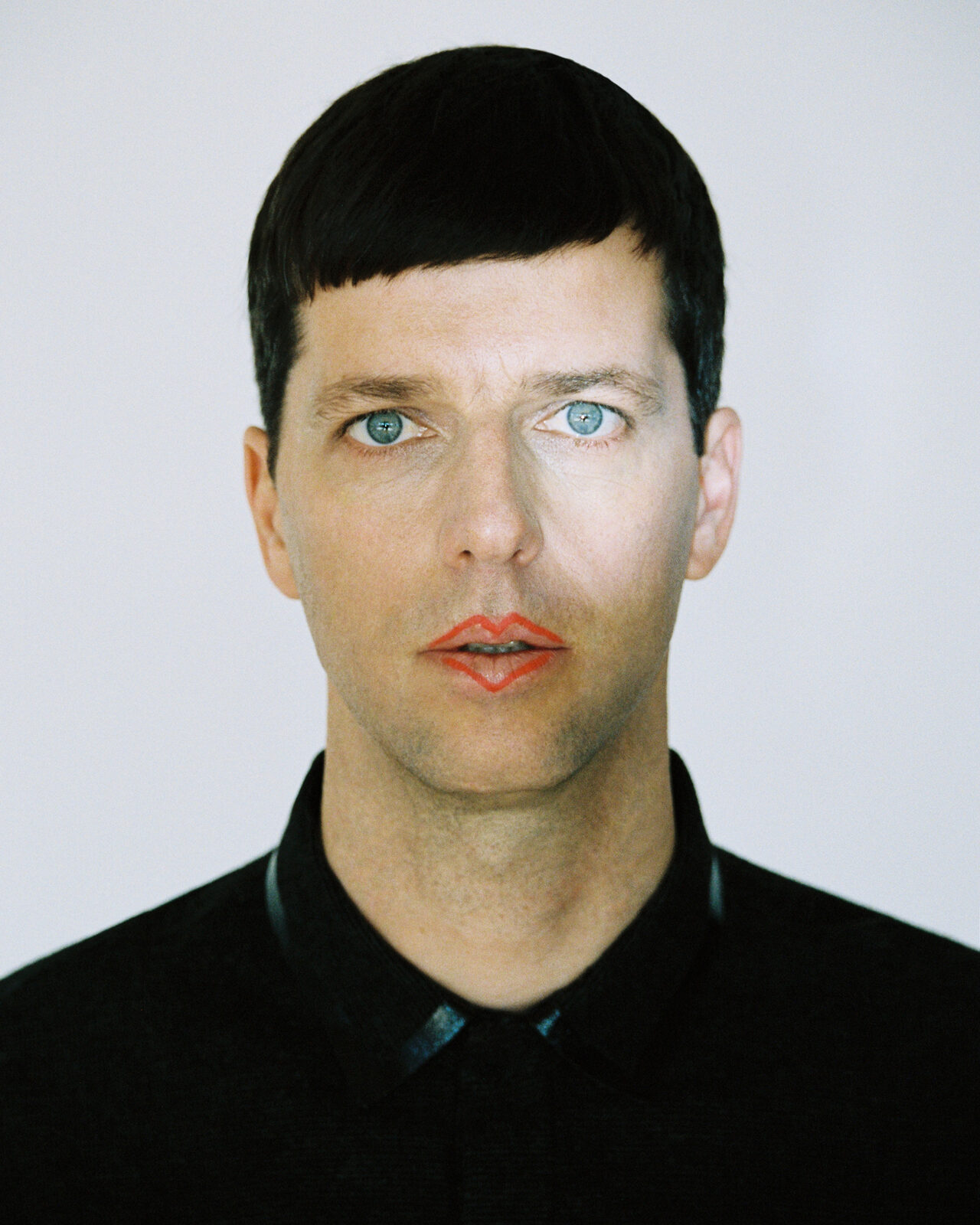 Studio portrait of Dixon facing the camera in a black collared shirt, with an outlined red lip design against a plain pale background
