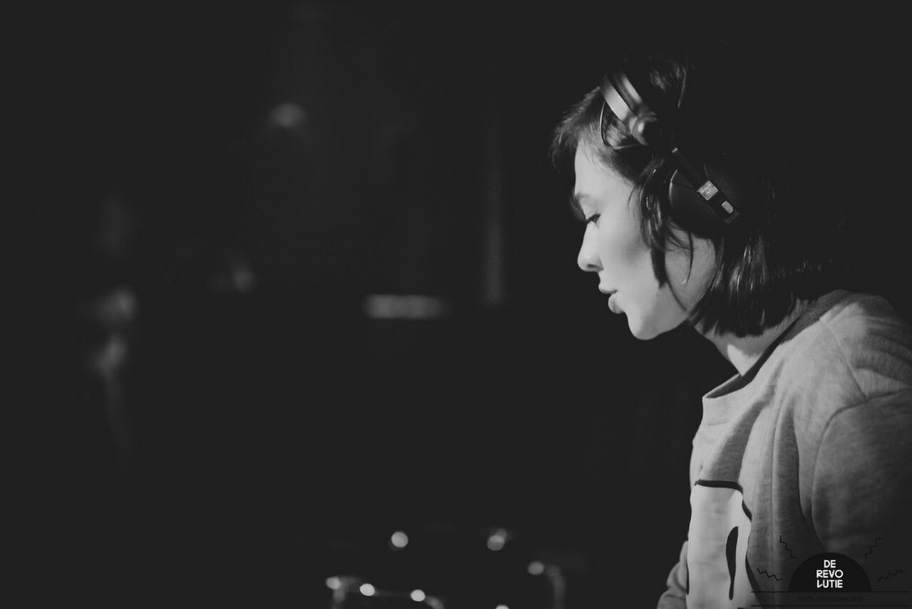 Nina Kraviz in profile wearing headphones, focused behind the decks at a club show