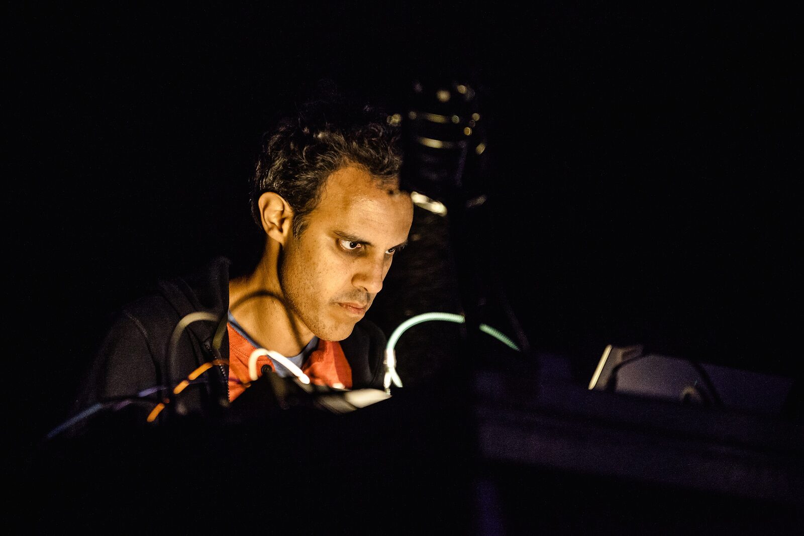 Four Tet looking down at his equipment on a dark stage, with cables in the foreground, at Roskilde Festival