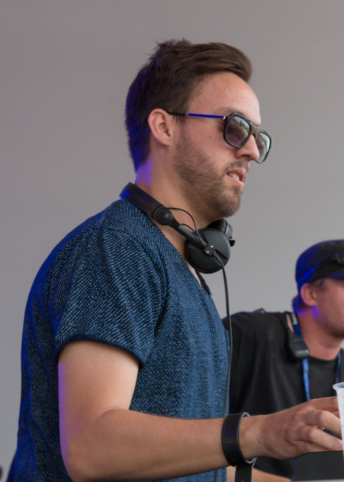 Maceo Plex in tinted sunglasses and a blue textured t-shirt with headphones around his neck, playing at Sea You Festival in 2015