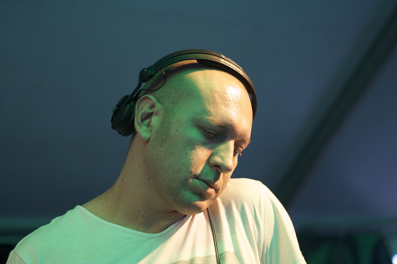 Marco Carola DJing with headphones around his neck under green stage lighting
