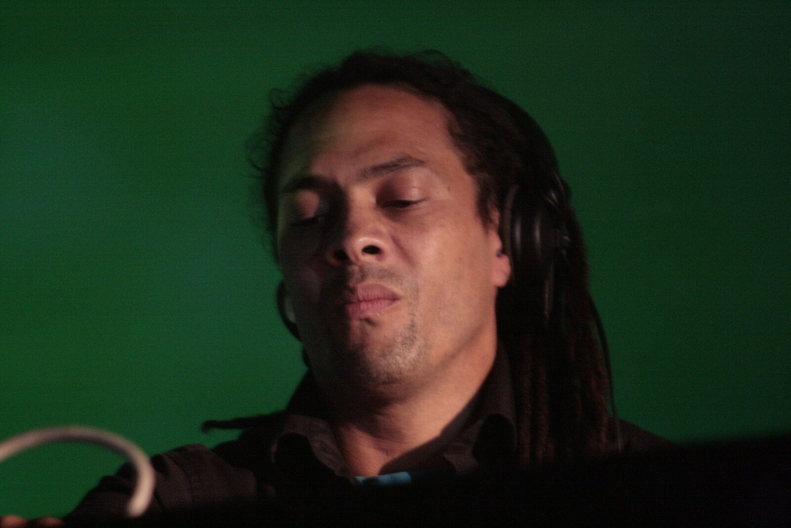 Roni Size performing a DJ set at Astropolis festival in Brest in 2009, headphones on, lit in green stage light