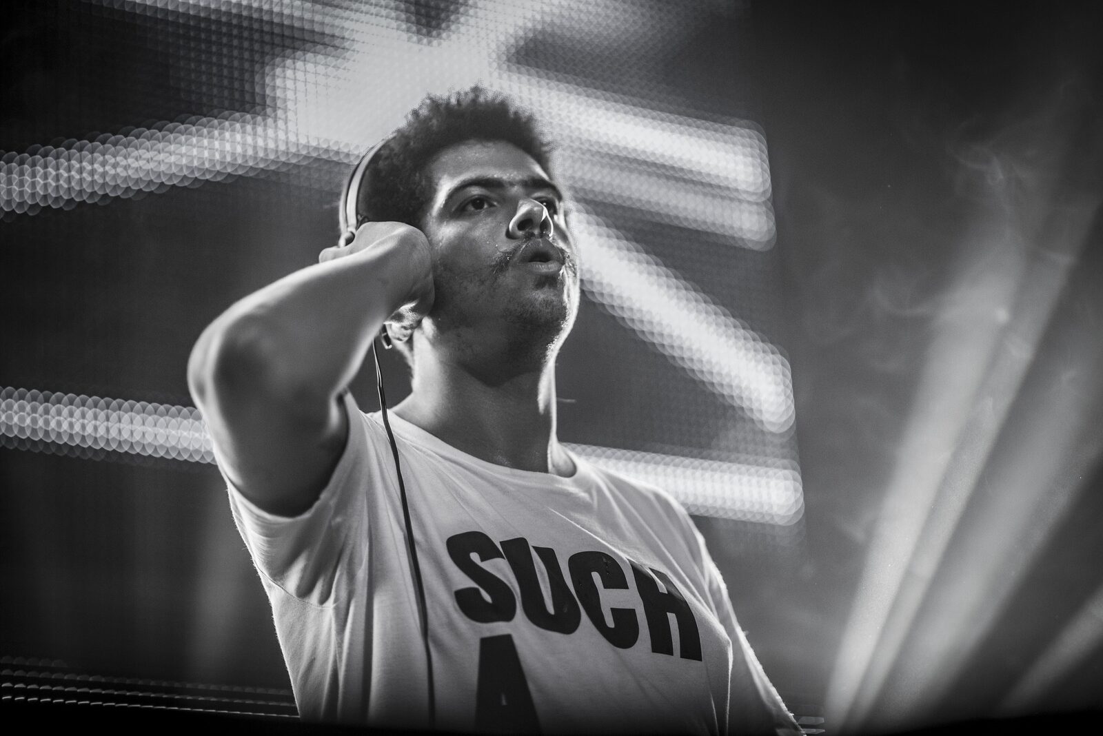 Black and white photo of Seth Troxler with one hand on his headphones, looking up from the DJ booth at Mint Festival in Leeds