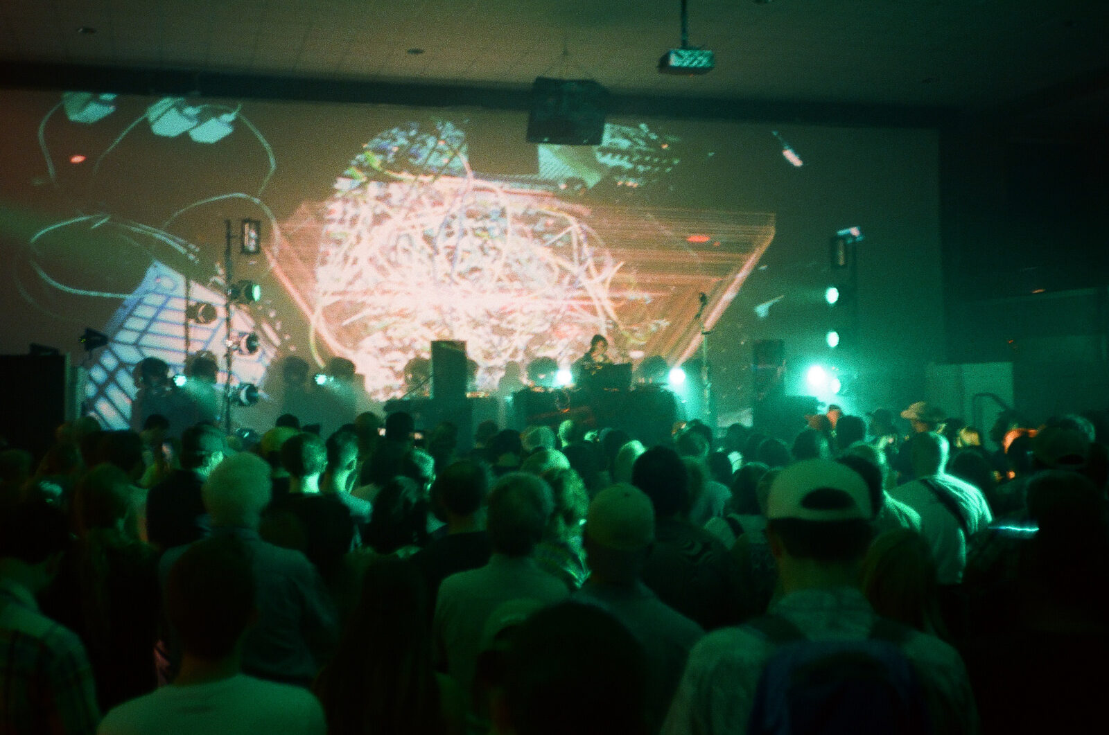 Suzanne Ciani performing at an electronic music concert at The Armory in Durham, North Carolina, in May 2017, with a crowd facing a stage lit green and projected visuals behind her.