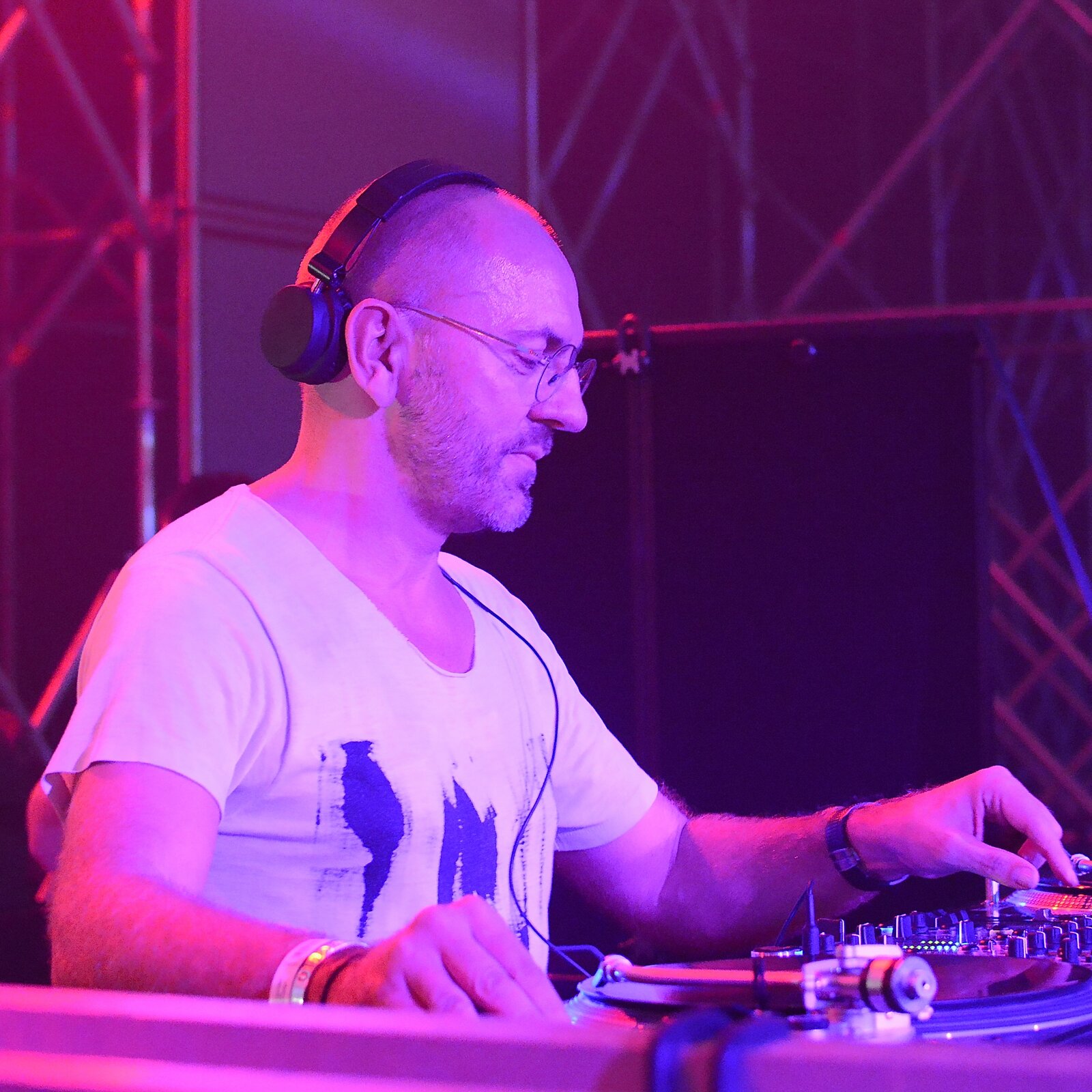 Sven Väth DJing in profile, wearing headphones and glasses under purple stage lighting