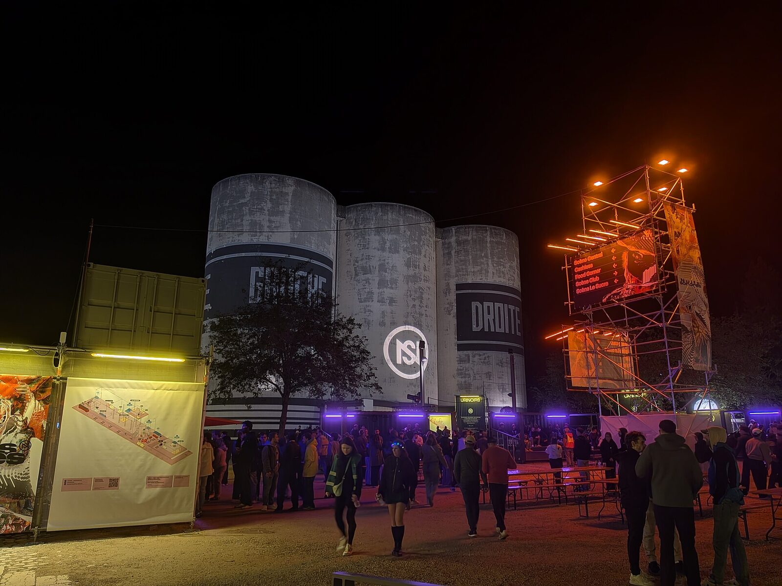 The silos of La Sucrière in Lyon lit at night with the Nuits Sonores logo during the 2026 edition, with festival-goers and signage in the foreground.