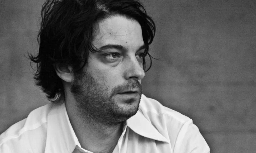 Black-and-white portrait of Kalabrese in a light collared shirt, looking off to the side against a plain backdrop